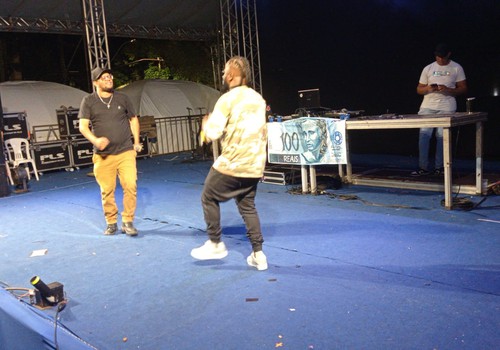 Com uma nota de R$100,00 ao fundo, rappers levam sua mensagem no palco da Fenapraça; veja ao vivo