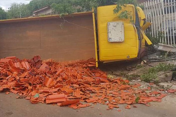 Caminhão carregado com telhas derruba poste, tomba e vai parar em grade de casa em Patos de Minas
